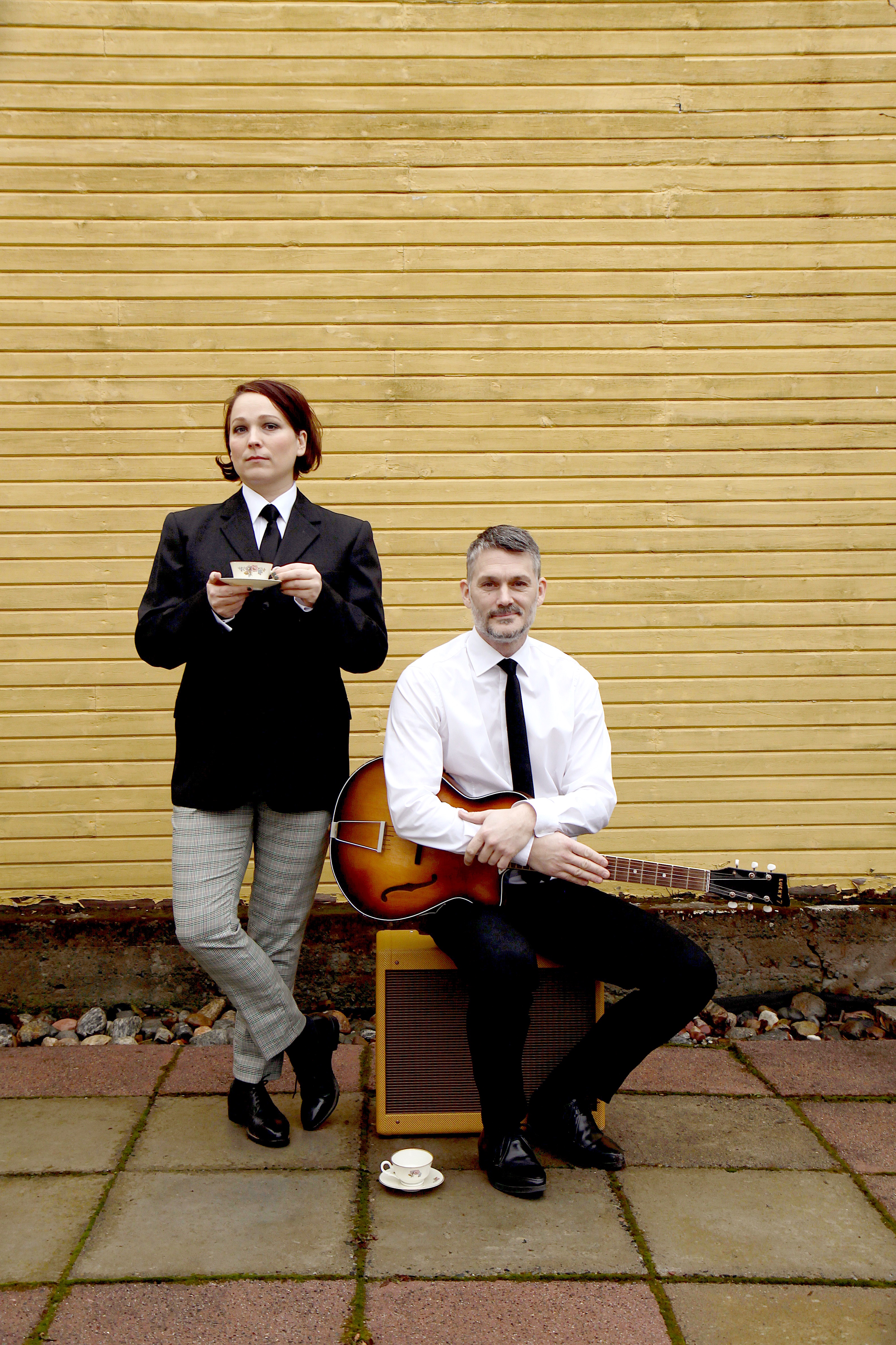 Två musiker iklädd Beatles kostym poserar med gitarr och tekopp