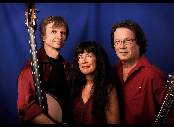 Tre musiker poserar med instrument framför blått tyg.