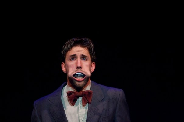 Man i kostym med ett munspel instoppat i munnen.